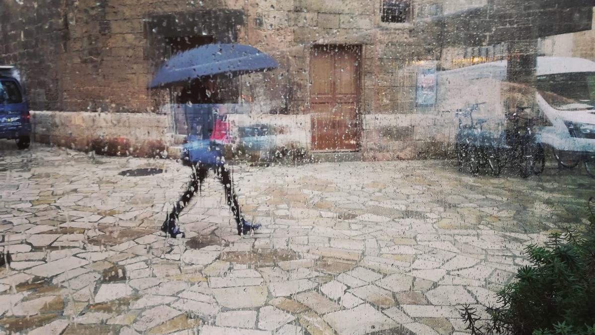 Archivo - Una mujer pasea por el centro de Palma con un paraguas, vista a través de un cristal con gotas de lluvia.