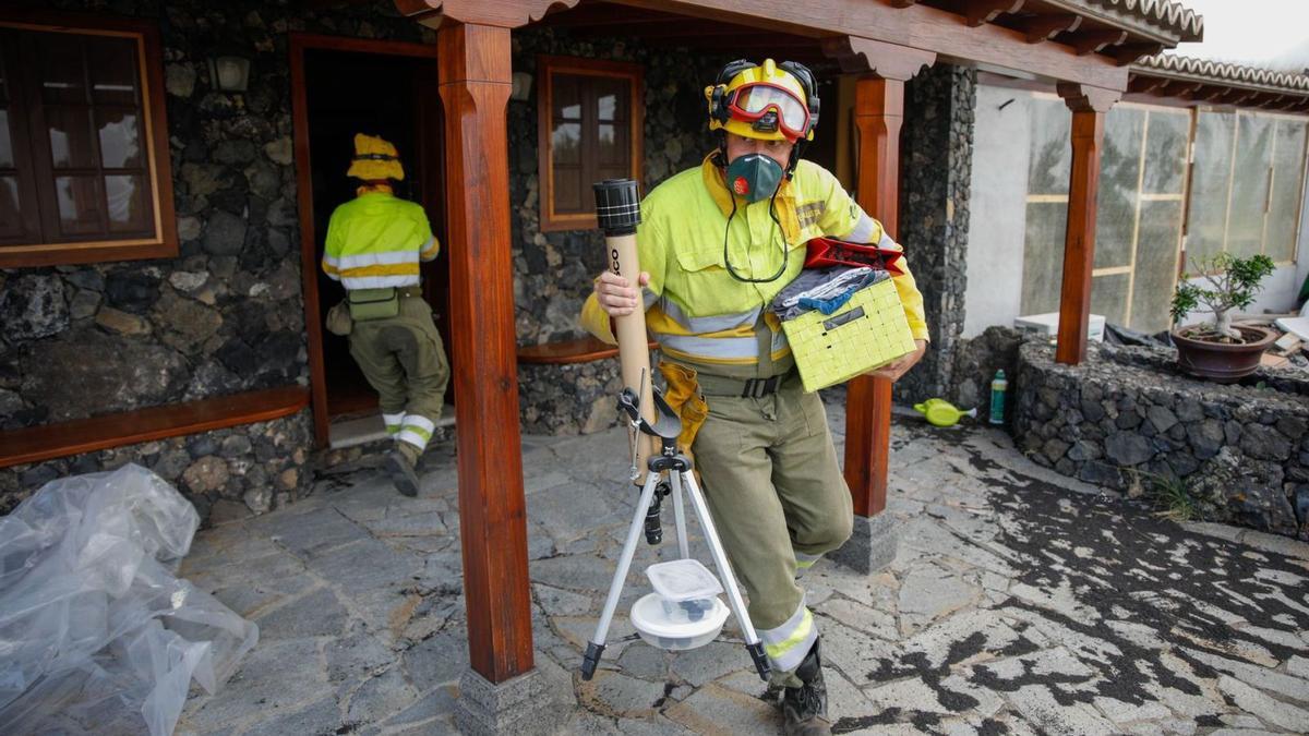 Dos bomberos ayudan a sacar enseres de una vivienda en La Palma.