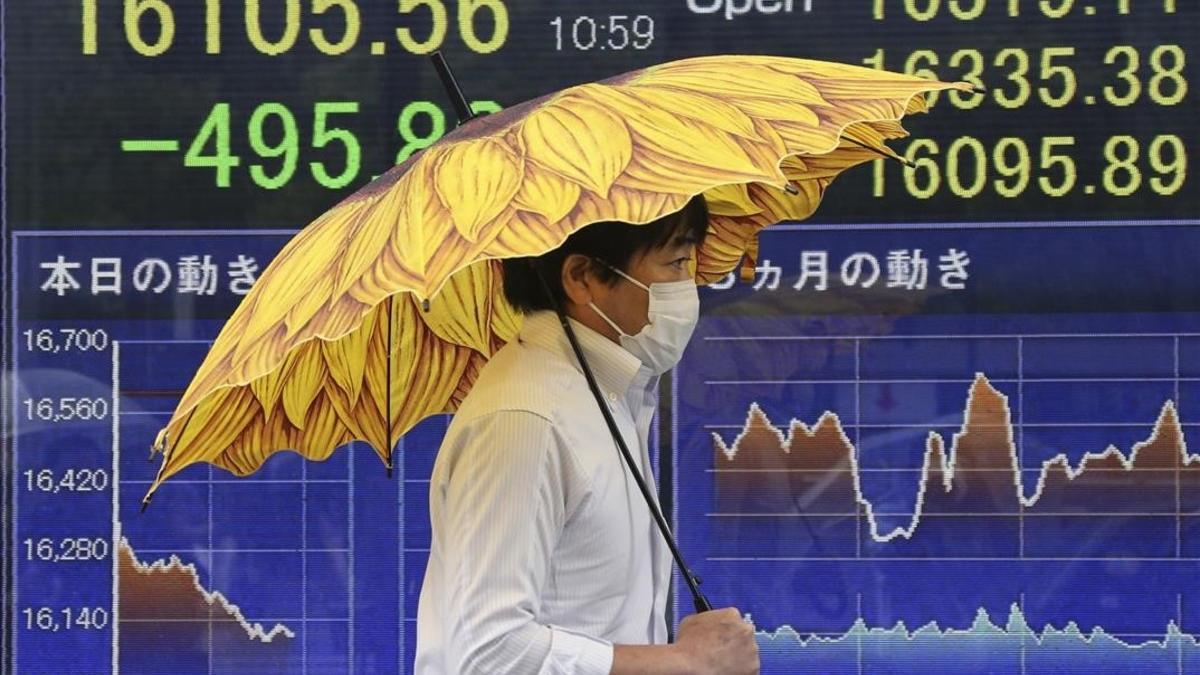 Un hombre pasa ante un sociedad de bolsa en Tokio en cuyo paneles informativos se muestra la caída del mercado.