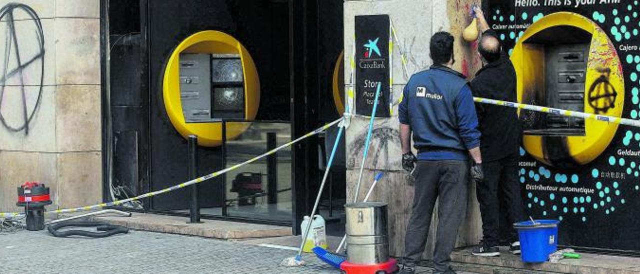 Operarios limpian varios cajeros vandalizados tras las protestas por Pablo Hasél en Barcelona.