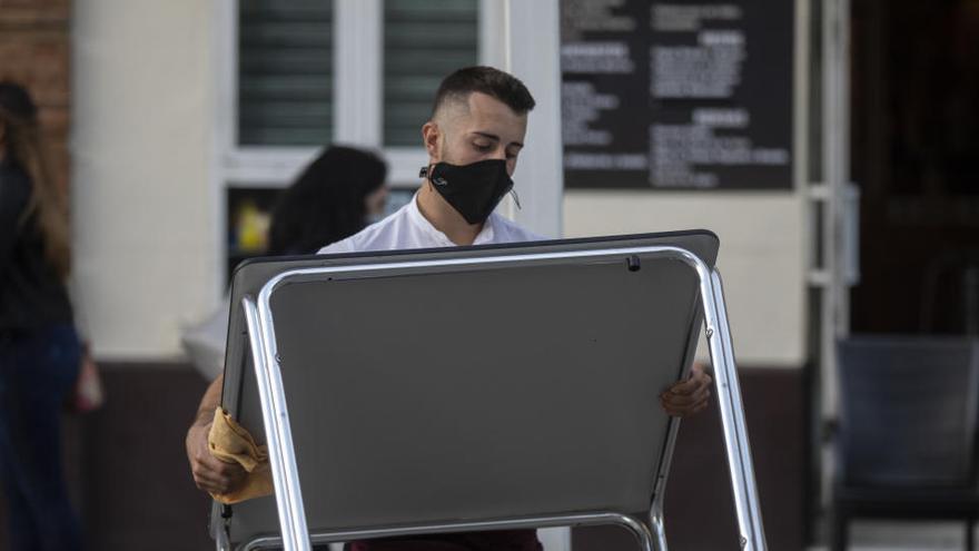 Un camarero recoge el mobiliario de la terraza de un bar.