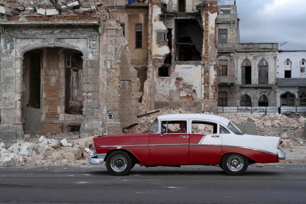 Un vehícuo circula junto a una vivienda con parte de su estructura derrumbada sobre la calle, en Centro Habana.