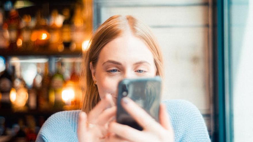 Una mujer consulta su teléfono móvil mientras sonríe.