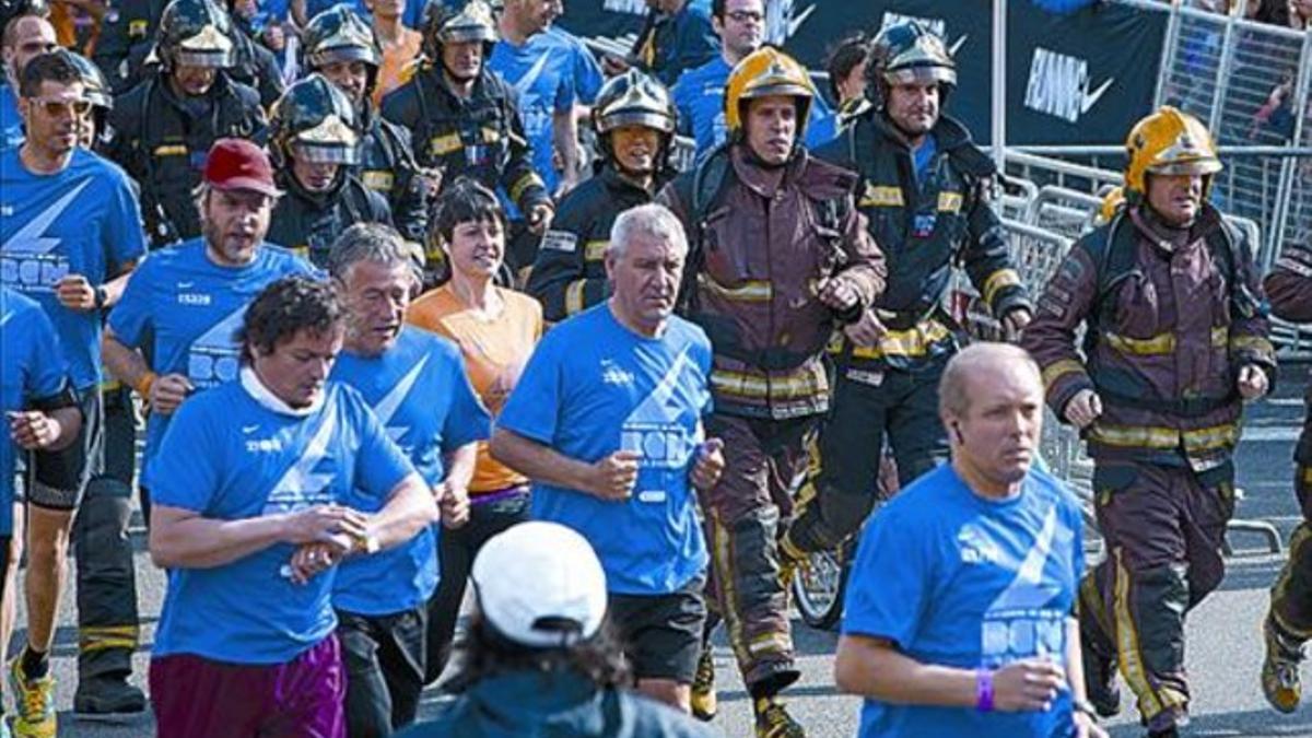 Bomberos, con ropa y material de trabajo, junto a otros atletas.