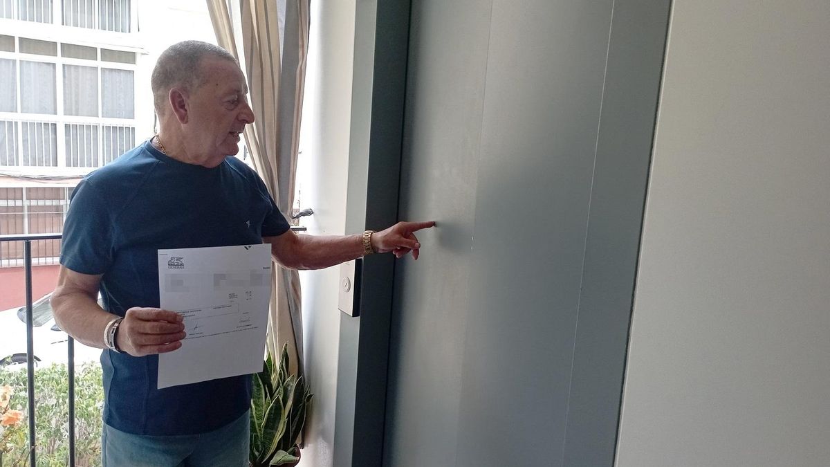 José Aguilar, con el ascensor del bloque y un documento de la compañía de seguros.