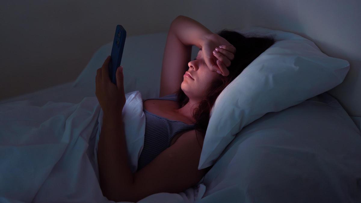 Una mujer consulta su teléfono móvil en la cama.