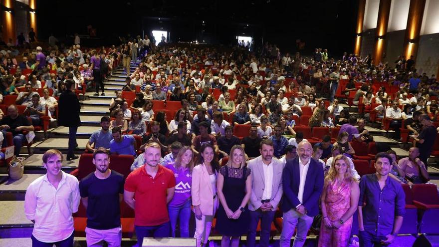 Primer plano de los participantes en la conferencia con el numeroso público detrás.