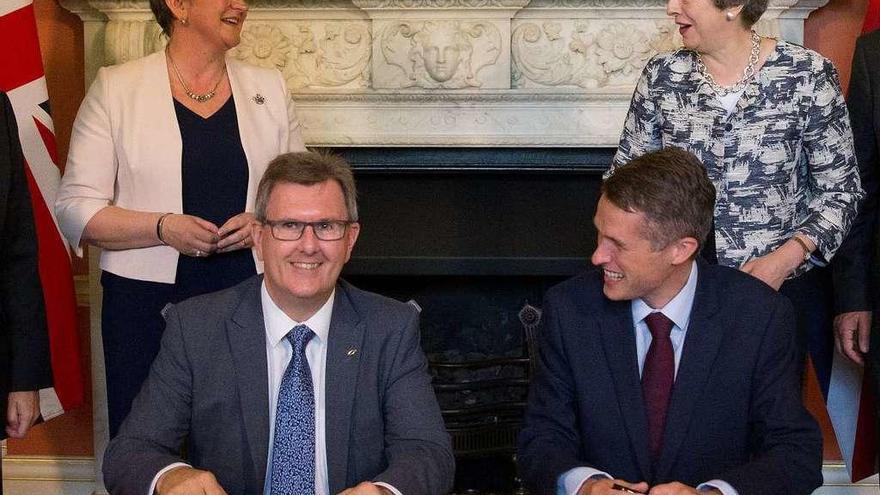 May (de pie, a la dcha.) y Arlene Foster, del DUP, presencian la firma del acuerdo de Gobierno por los parlamentarios &quot;tory&quot;, Gavin Williamson, y unionista, Jeffrey Donaldson (sentado, a la ida). // Reuters