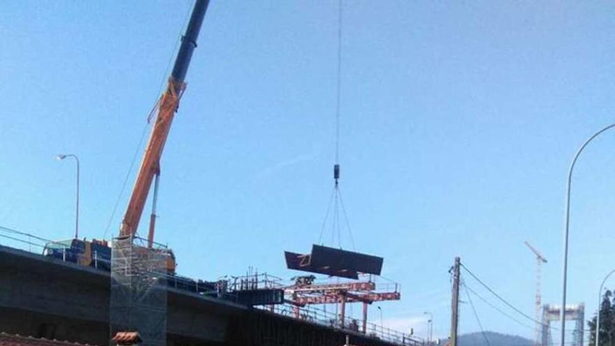 Una grúa traslada material al puente de Rande por encima de las casas.