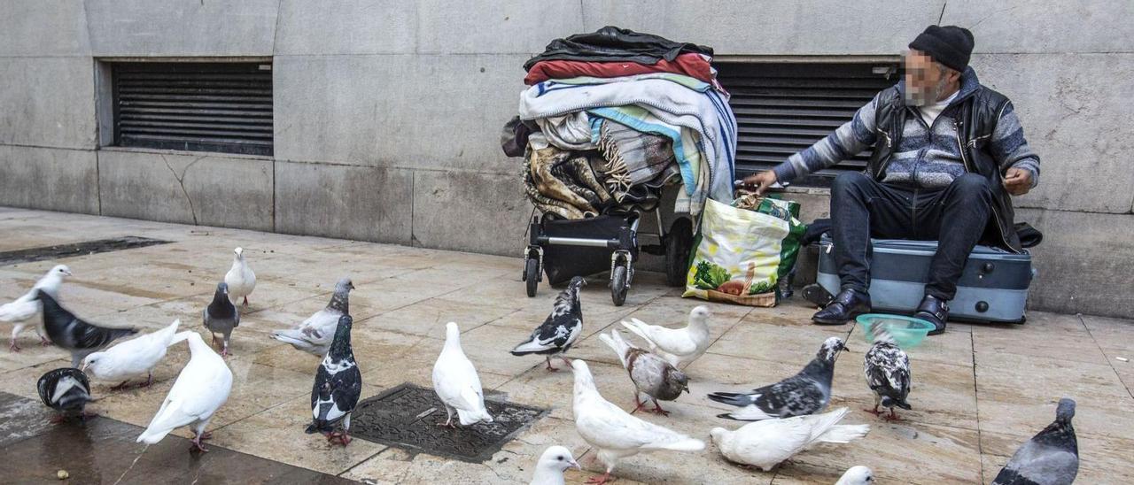 Un hombre pide dinero en una calle de Alicante, junto a sus pertenencias. | ALEX DOMÍNGUEZ
