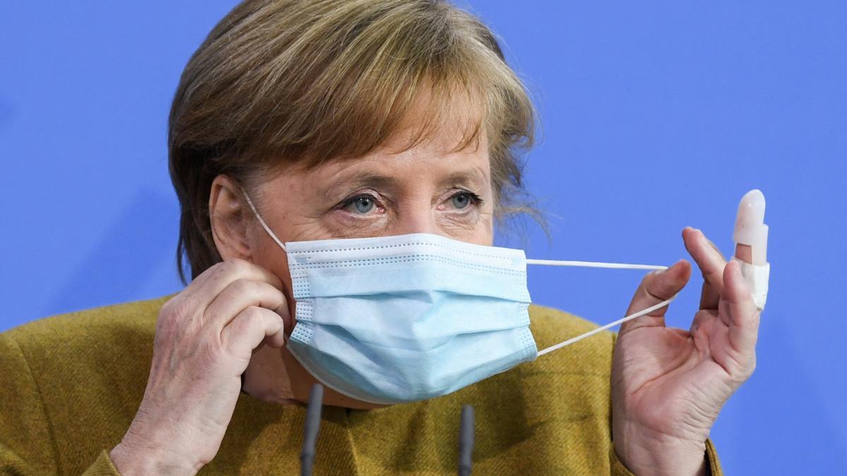 La cancillera alemana, Angela Merkel, se retira la mascarilla antes de la comparecencia que ha ofrecido este martes para explicar el proyecto de ley aprobado por el Gobierno.