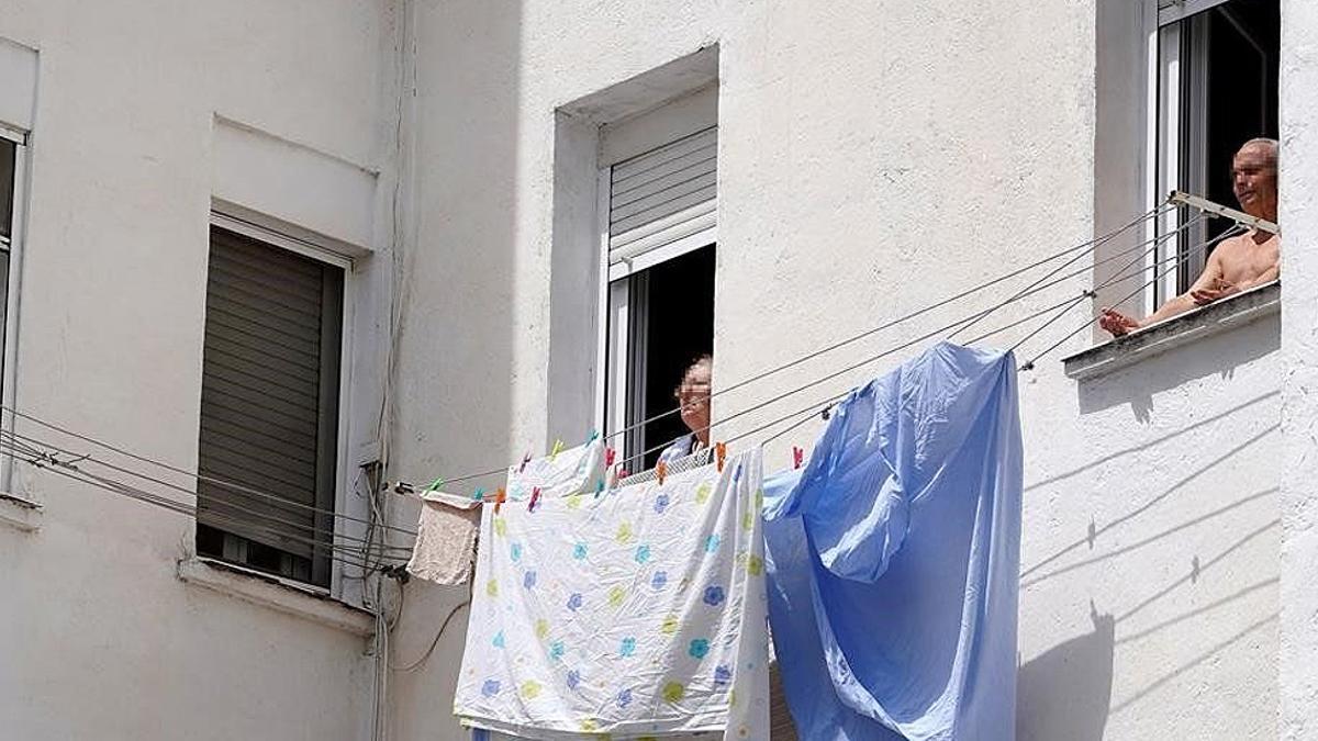 Dos personas mayores toman el sol en la ventana vivienda en Madrid.