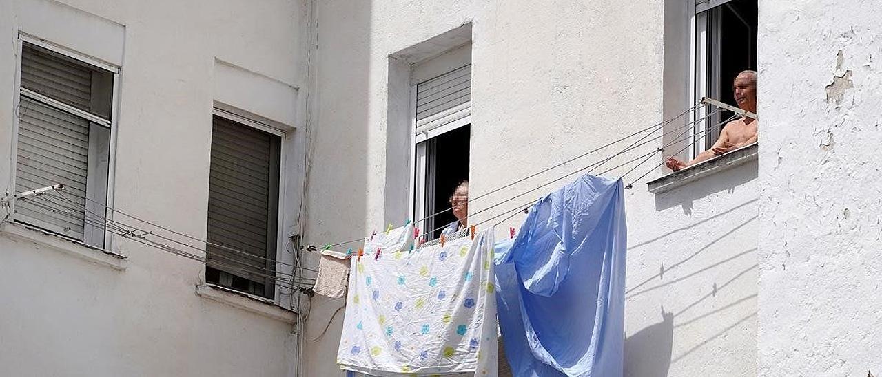 Dos personas mayores toman el sol en la ventana vivienda en Madrid.