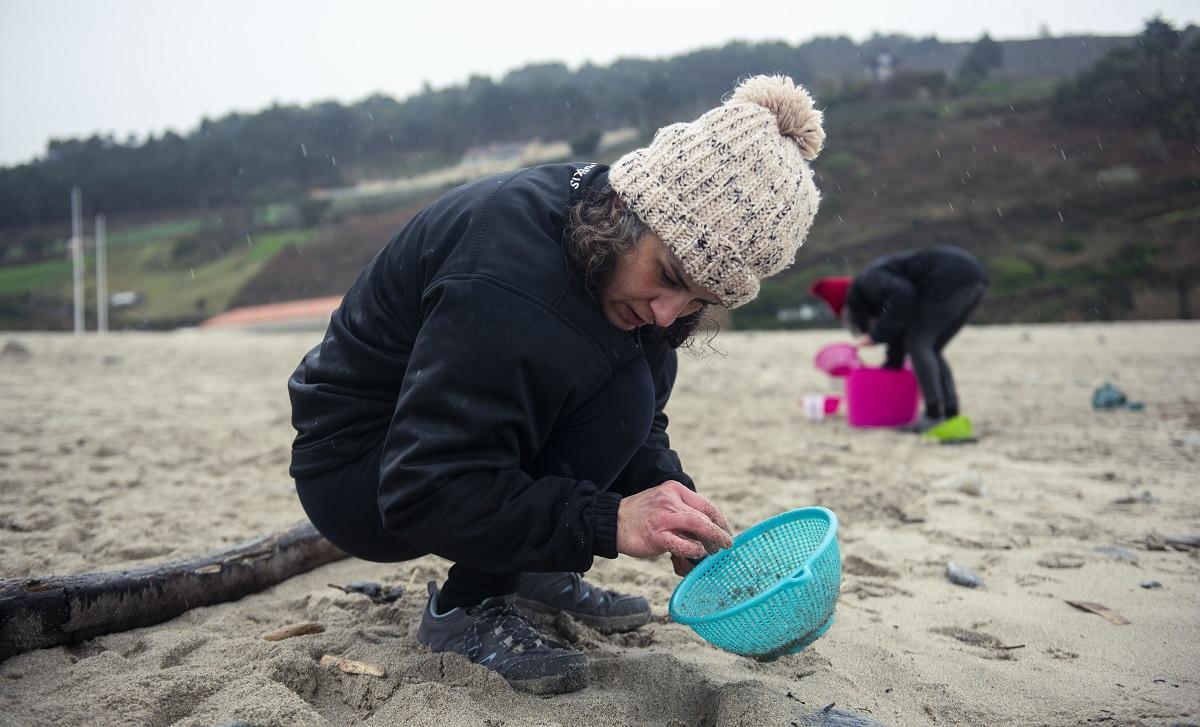 Una voluntaria retira pellets en el arenal de la playa de Valcobo