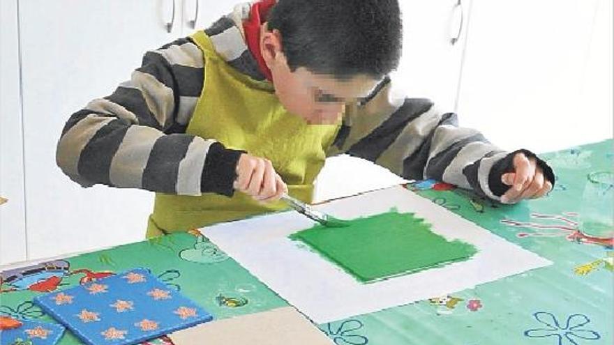 Un niño autista del centro El Cau de Castelló pintando una tabla en el taller de manualidades.