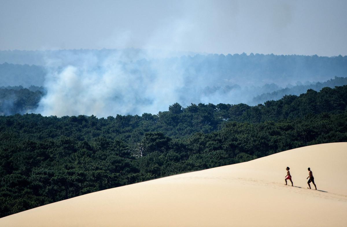 Gente camina por la duna de Pilat, cerca de La Teste-de-Buch, en el sudoeste de Francia, el 16 de julio del 2022. Al fondo, uno de los fuegos que afectó a la región.