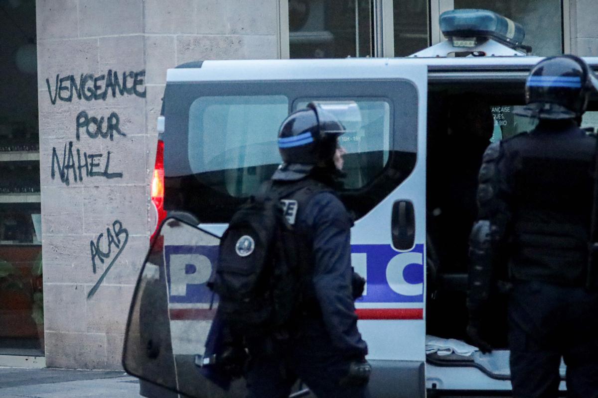 Los disturbios se extienden por Francia en la cuarta noche de protestas. La policía antidisturbios francesa hace guardia cerca de un grafiti que dice venganza por Nahel durante una manifestación en Caen, noroeste de Francia