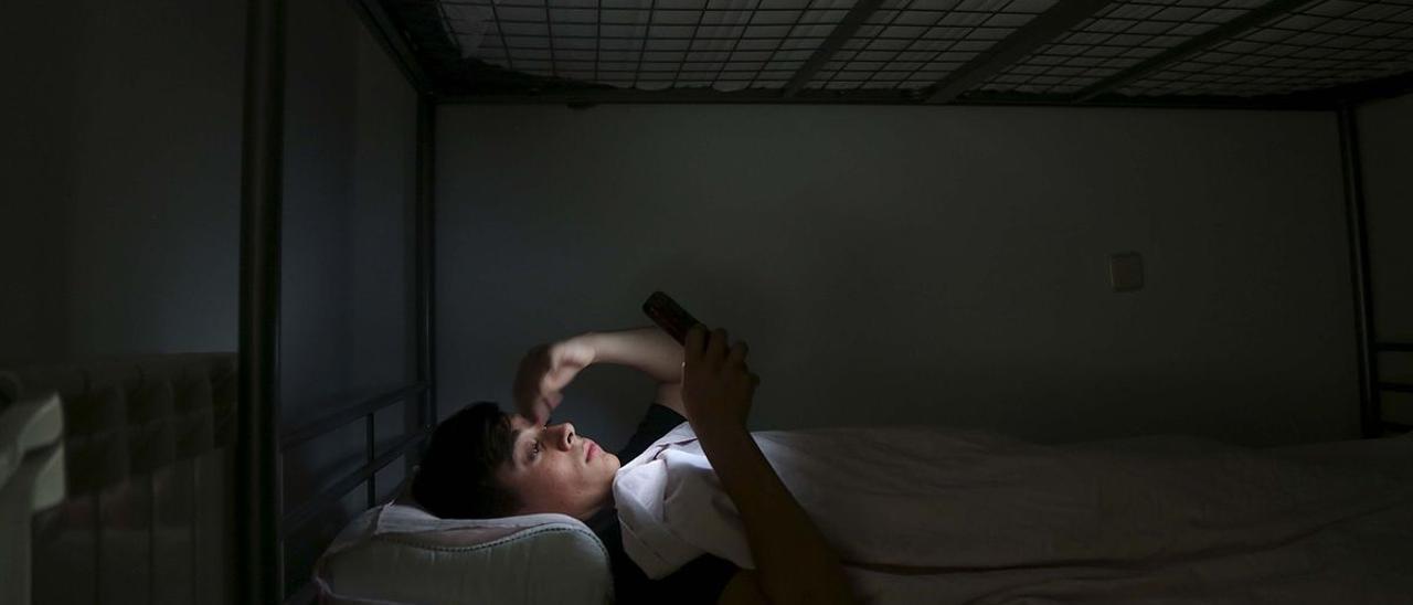 Un adolescente consulta su teléfono móvil en el dormitorio.
