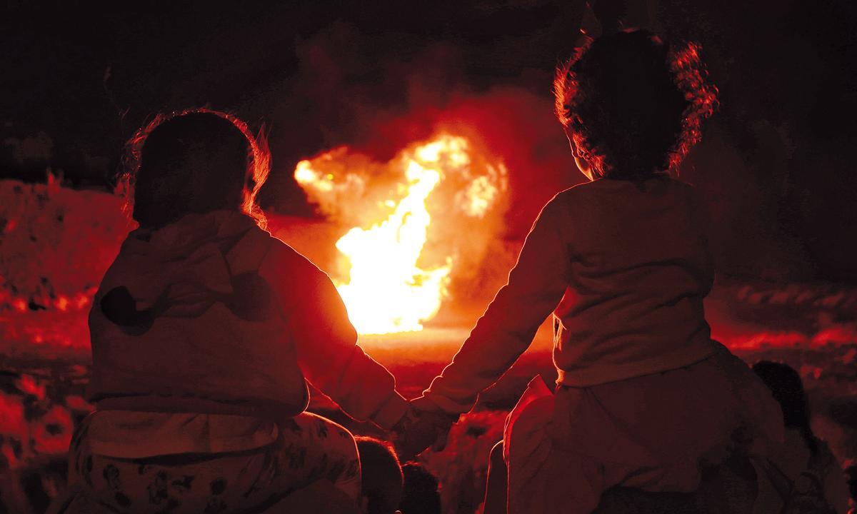 Dos niños observan una hoguera en la verbena de Sant Joan.