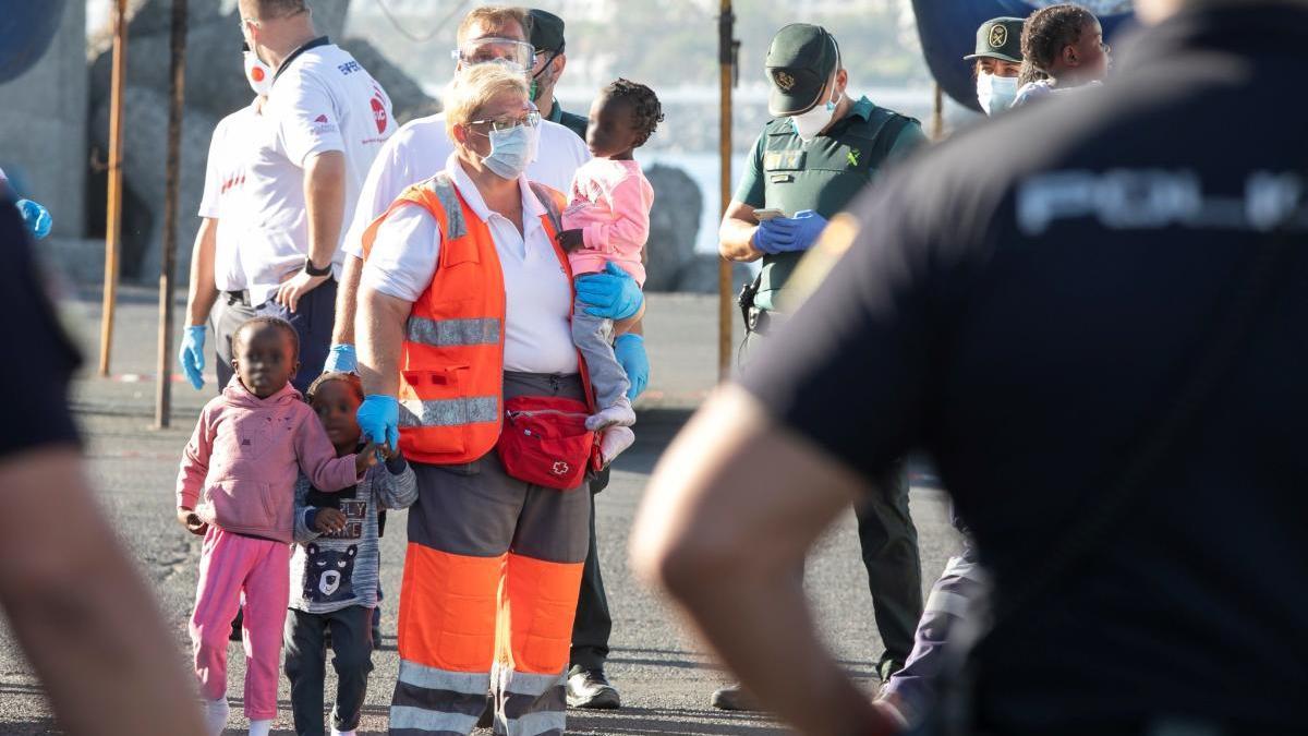 La voluntaria de Cruz Roja María Afonso sujeta en el puerto de Arguineguín (Gran Canaria) a tres niños rescatados por Salvamento Marítimo el 20 de mayo de 2020 de una patera, tras proporcionarles algo de comida y ropa seca