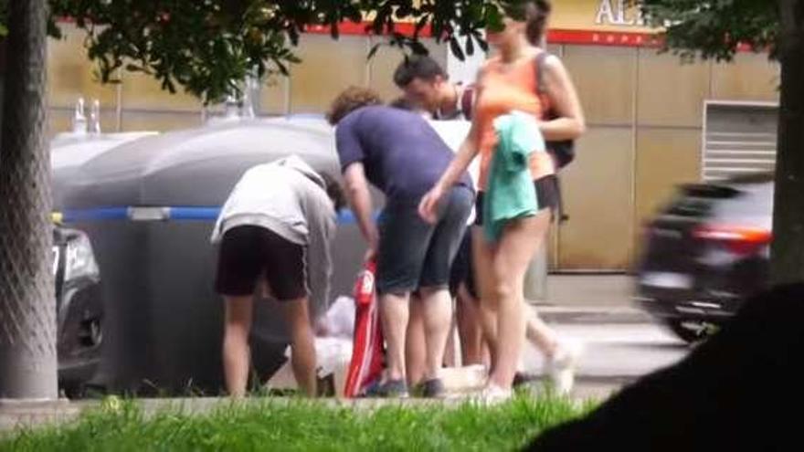 El actor Roca Suárez, de espaldas con camiseta oscura, enseña a varios viandantes la camiseta que decía haber hallado junto a un contenedor.