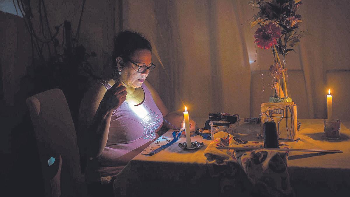 Roxana cose en el salón de su casa con velas, para ahorrar en electricidad dada su situación de precariedad.