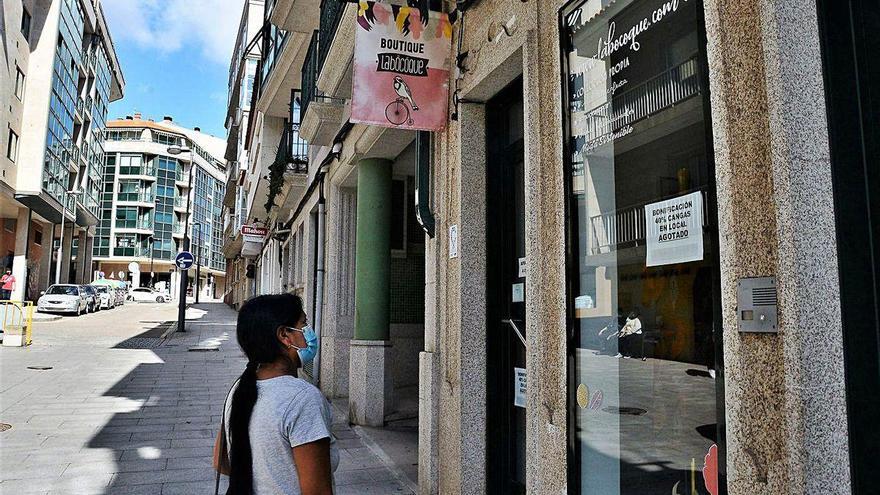 Una mujer observa el escaparate de un comercio de Cangas con el cartel de "bono agotado".