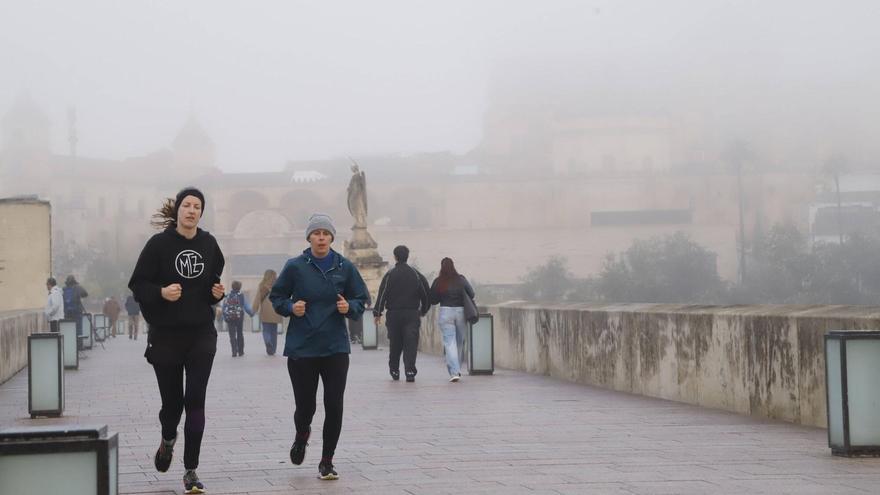 Varias personas hacen deporte por el Puente Romano de Córdoba bajo una densa niebla.