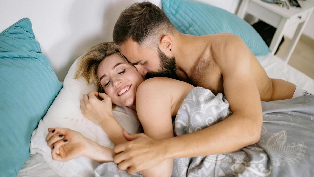 Un hombre huele y besa a su pareja en la cama.