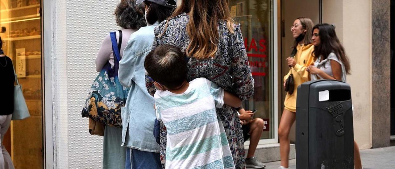 Un niño abraza a su madre mientras esperan para entrar en un comercio, en Madrid.
