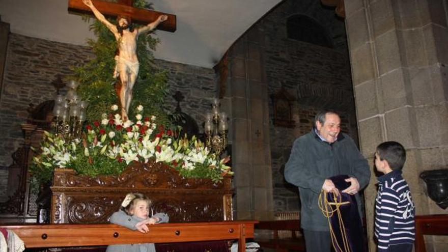 Ramón Jesús Suárez guarda la túnica de su nieto, Pablo Rodríguez, observado por la pequeña María da Costa, frente a la imagen del Cristo del Perdón, ayer, en Luarca.