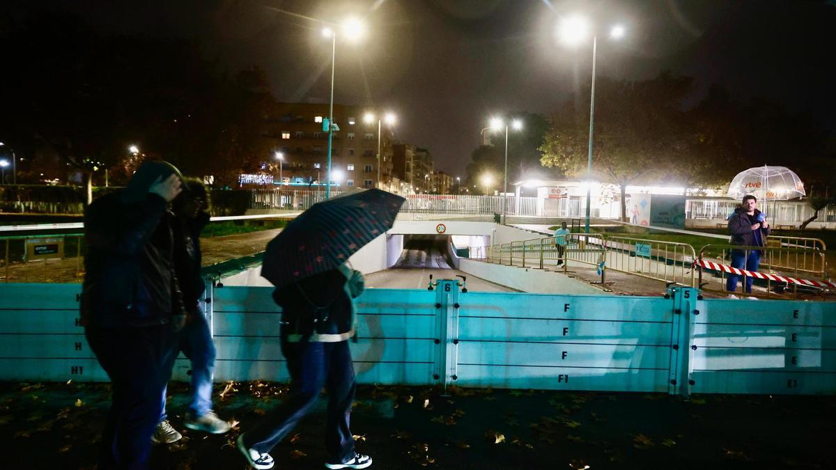 Vecinos con paraguas pasean frente a las barreras de contención de Aldaia.