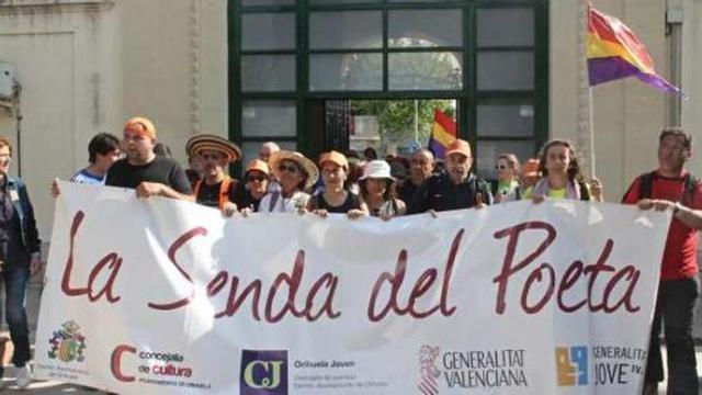 Los senderistas posan con la pancarta que abría la marcha a su llegada al cementerio.
