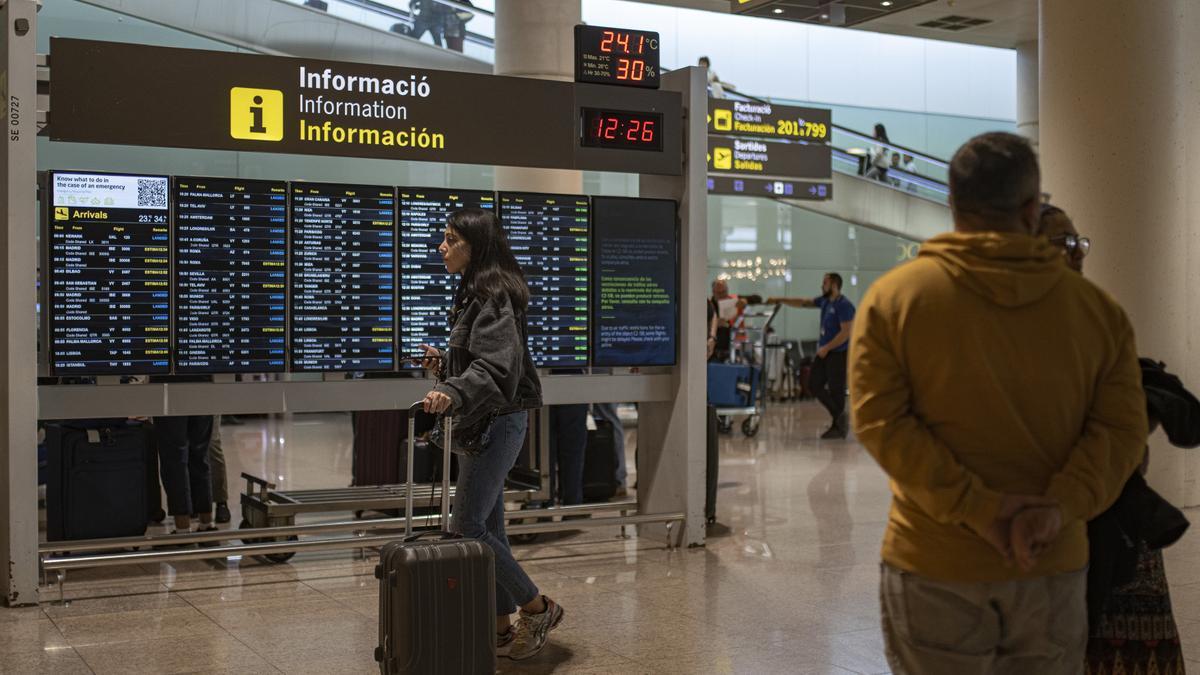 Varias personas observan un panel de llegadas en el aeropuerto de Barcelona.