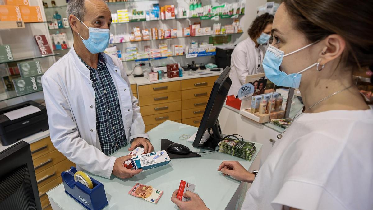 Un farmacéutico atiende a una clienta en una farmacia de Alicante