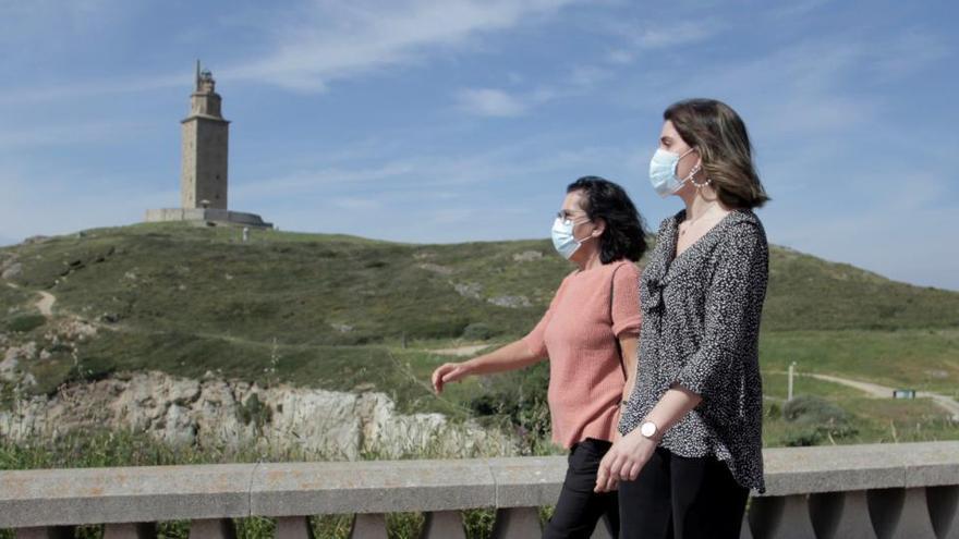 Dos mujeres con mascarilla caminan cerca de la Torre de Hércules.