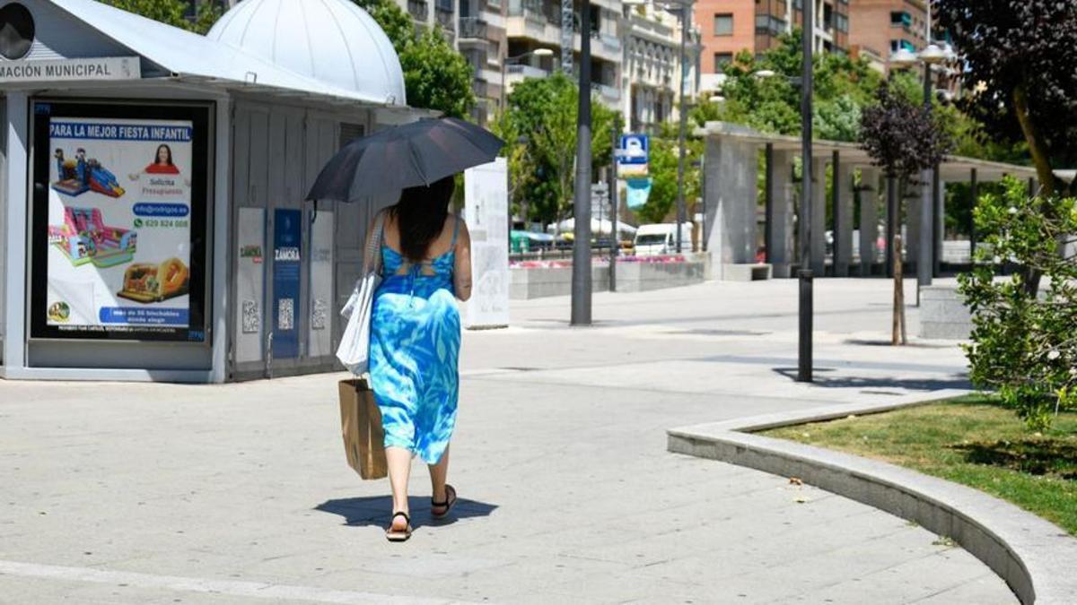 Una mujer se protege con un paraguas del sol en la plaza de La Marina.