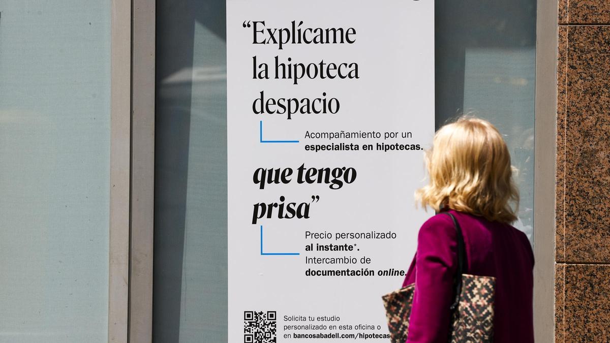 Una mujer pasa frente al escaparate de un banco que publicita hipotecas.