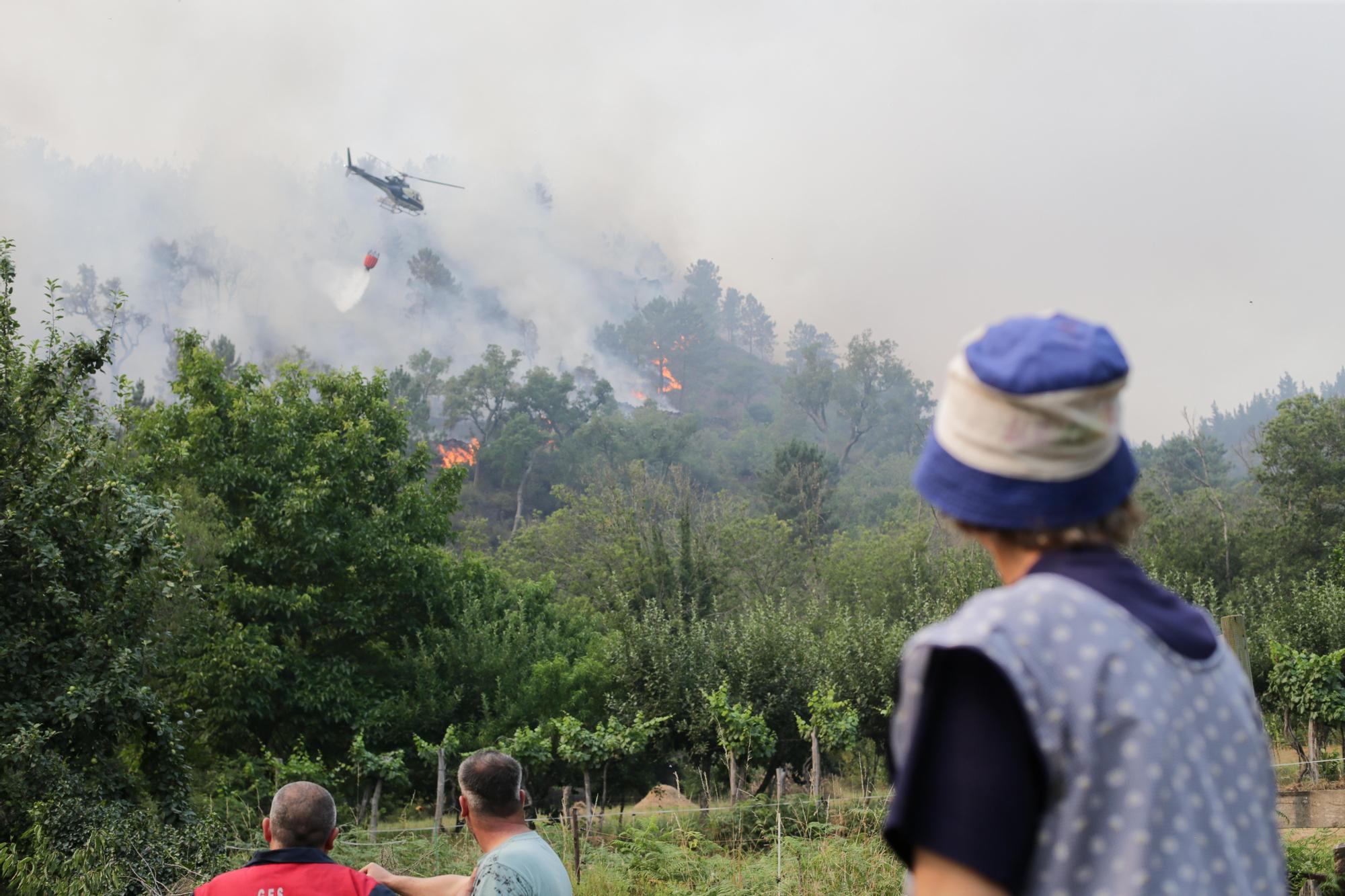 Varias persoas observan como un helicóptero trata de extinguir un lume nas inmediacións dun incendio en Quiroga. Foto de arquivo.