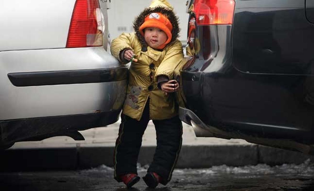 Un nen juga entre dos cotxes aparcats en un carrer de Pequín (Xina).