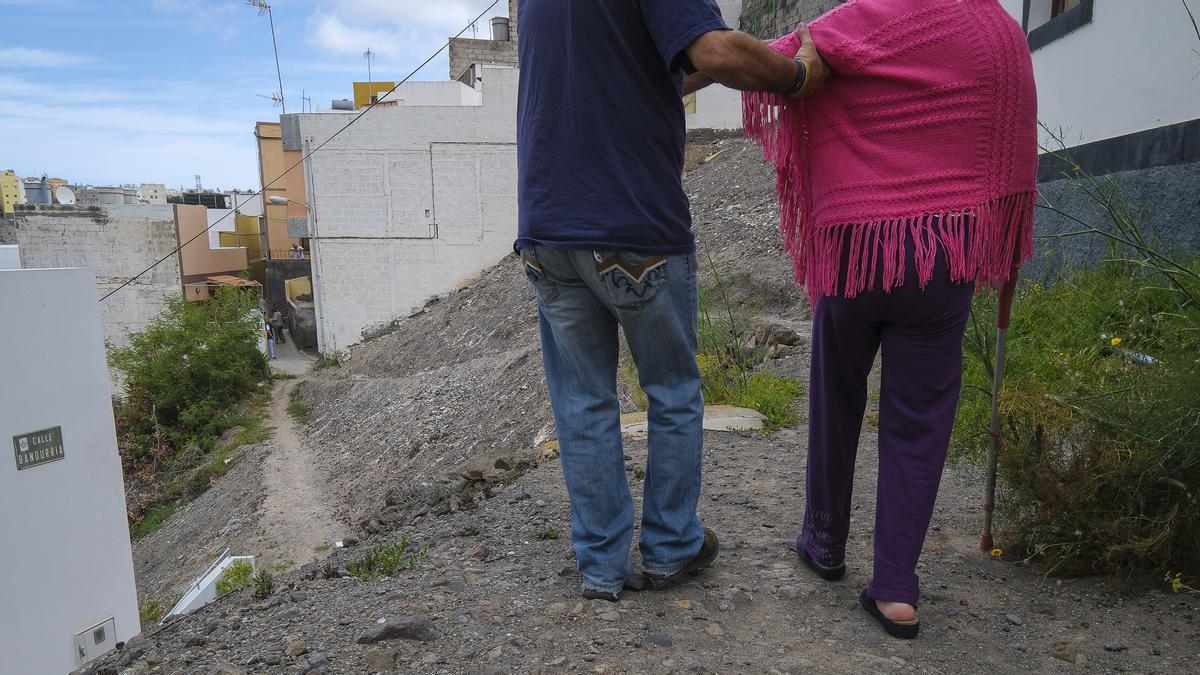 Un vecino ayuda a una mujer con movilidad reducida a pasar por la calle Bandurria.