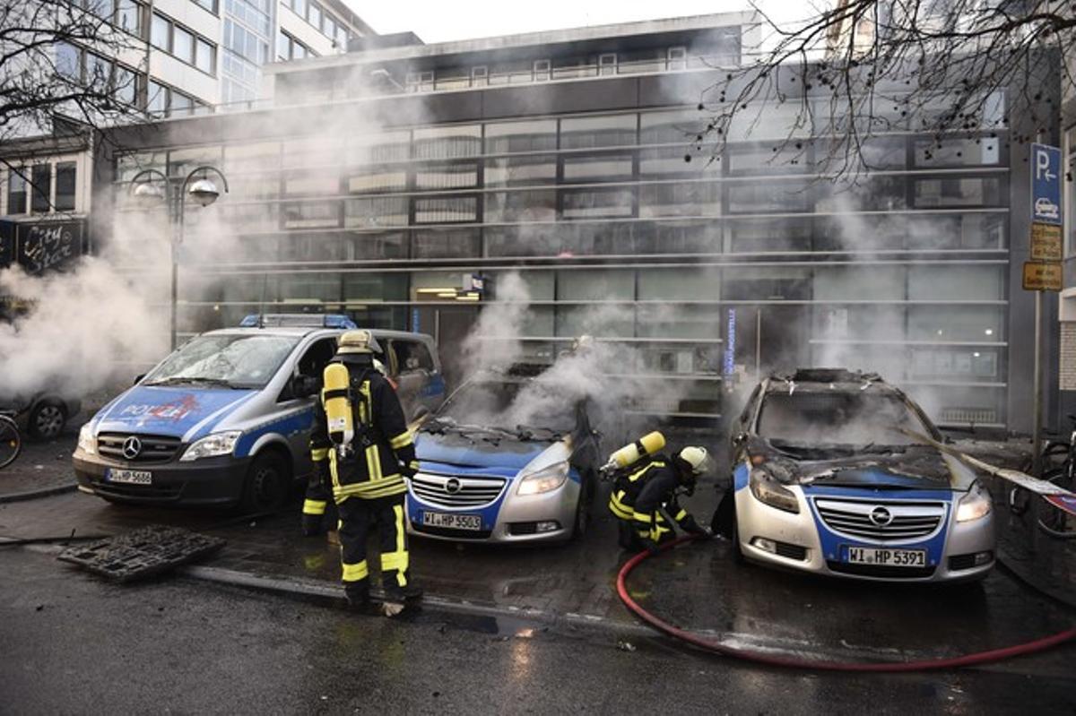 Los bomberos tratan de extinguir las llamas de varios coches de policía incendiados.