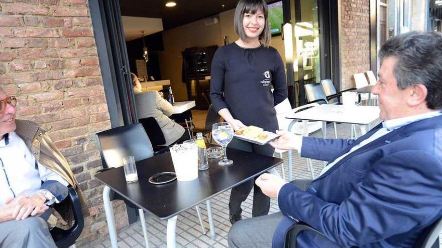 Priscila de Souza, sirviendo un pincho de tortilla a Amalio Suárez en una terraza de El Entrego.