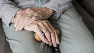 Una persona mayor apoya sus manos en un bastón. 