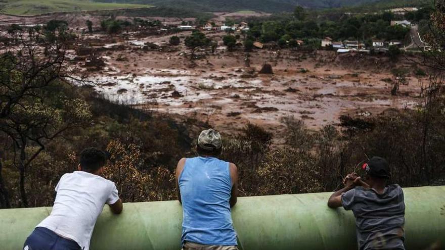 Tres personas contemplan el distrito de Bento Rodrígues, prácticamente sepultado por el lodo.