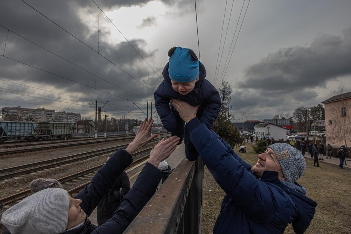 Un padre ucraniano que decidió no abandonar Irpin pasa a su hijo por encima de una verja para entregárselo a su mujer antes de la llegada de un tren de evacuación a la estación de Irpin, el 4 de marzo de 2022. 