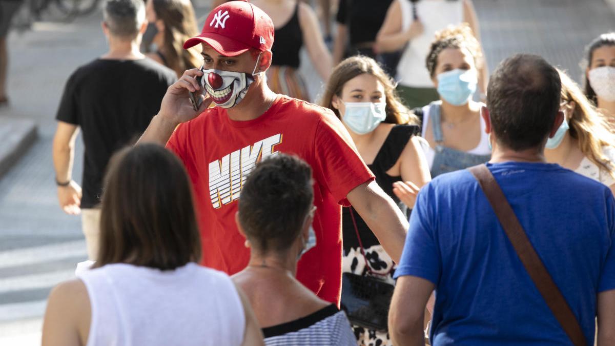 Un joven pasea por la calle Colón ataviado con una mascarilla con sonrisa de payaso.