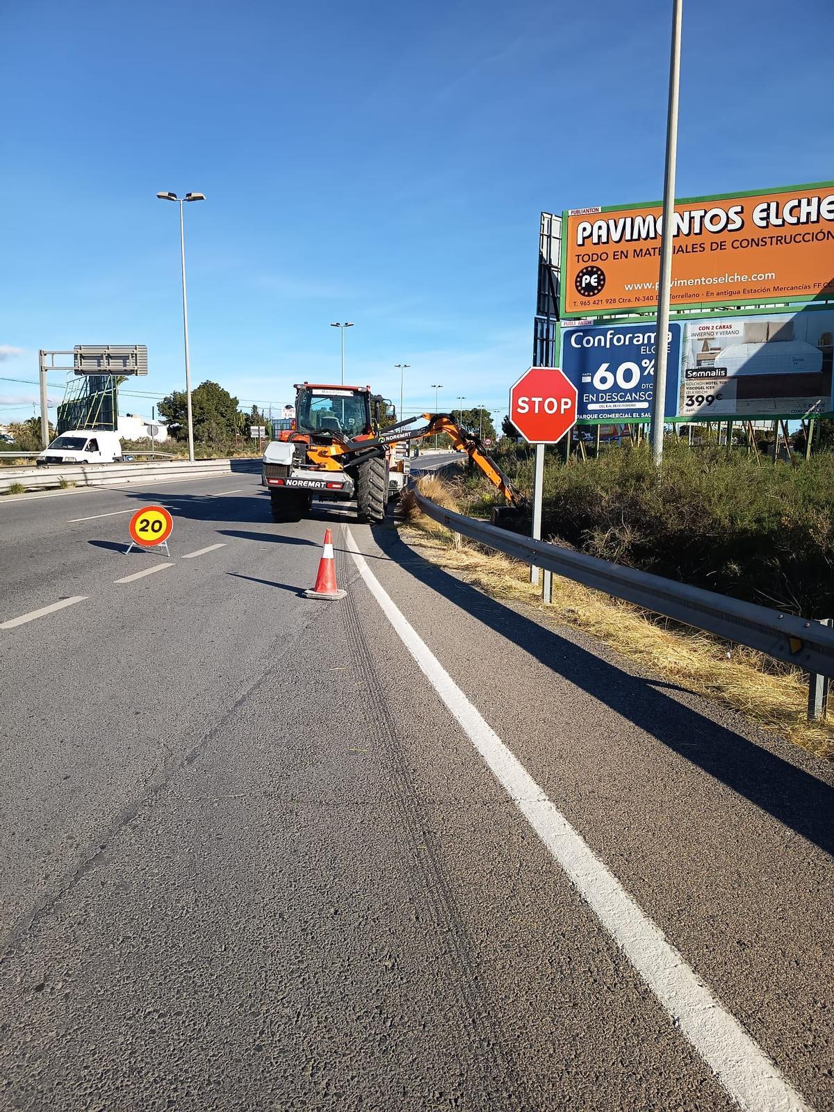 Una máquina desbrozadora quitando hace días la maleza del borde de la carretera que tapaba la visión