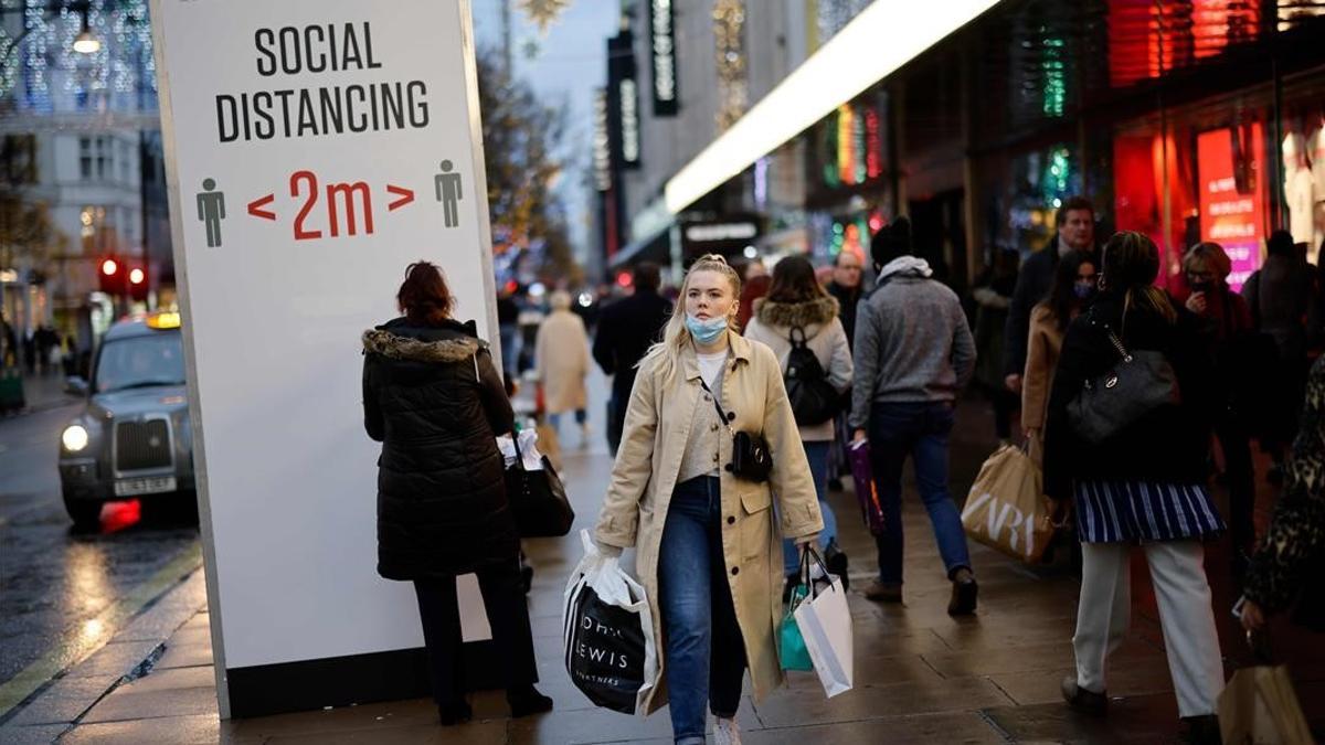 Una mujer pasea por la céntrica Oxford Street, en Londres, entre carteles que piden distancia social.