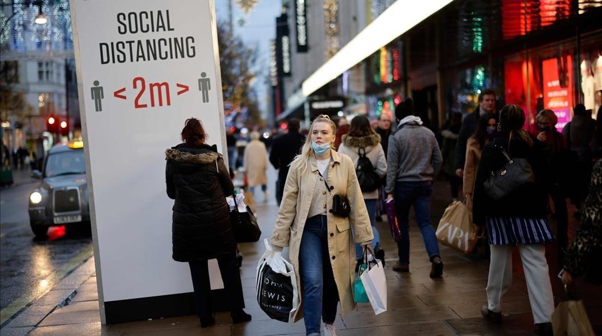 Shoppers and pedestrians walk past a sign advising social distancing in Oxford Street in central London on December 14  2020  as it is announced that Greater London will be moved into Tier 3 from Tier 2 from Wednesday December 16  - London is to move into the highest level of anti-virus restrictions  the health minister announced Monday  The British capital from Wednesday will go into  tier three  restrictions  which force the closure of theatres and ban people from eating out at restaurants or drinking in pubs  the Health Secretary Matt Hancock told parliament  (Photo by Tolga Akmen   AFP)